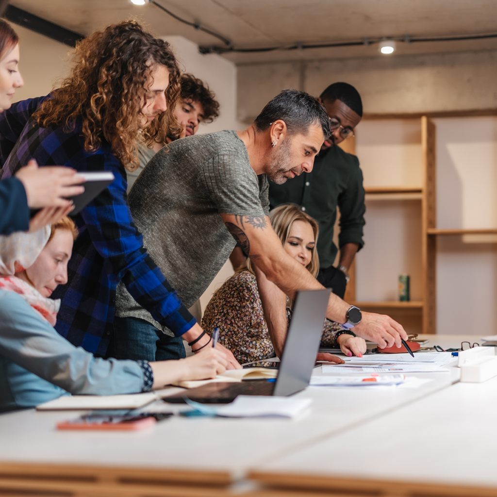 A group of people sitting around a table with laptops.